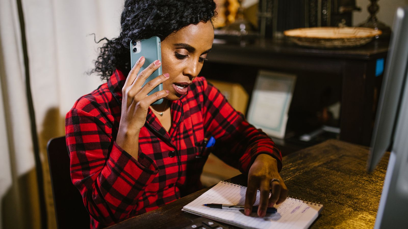 A writer on a phone call, finger on her notebook, checking a figure as she asks about it.